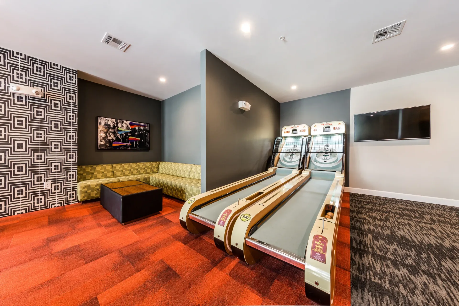 Community game room with skeeball machines, sectional sofa, and TV.