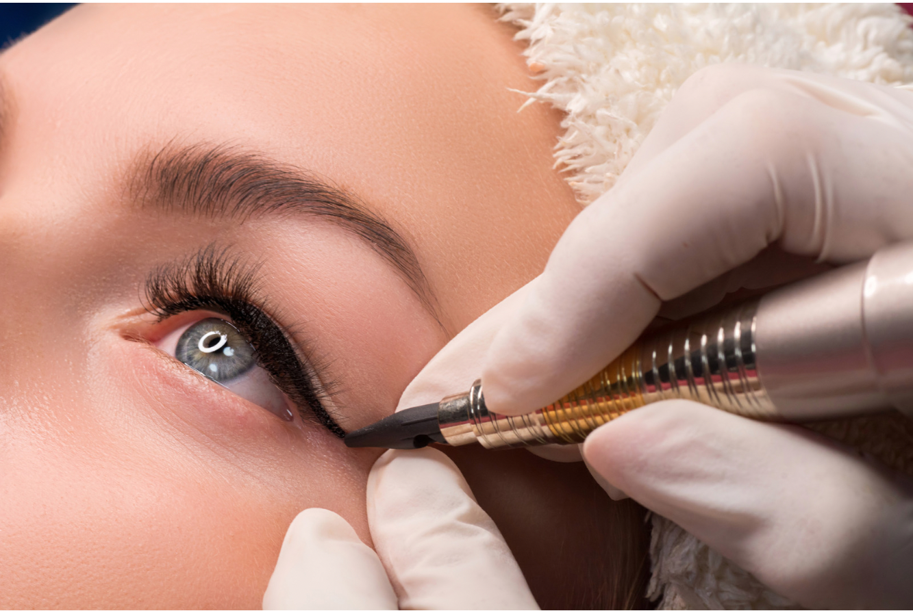 Woman receiving permanent eyeliner on her eyelid. Close-up shot shows hand in glove holding machine.
