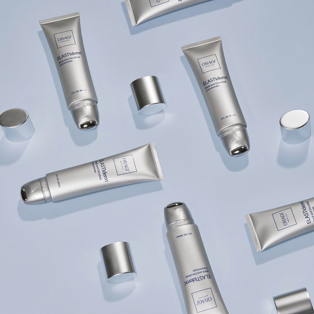 Silver tubes of eye cream, caps off, scattered on a light blue background.