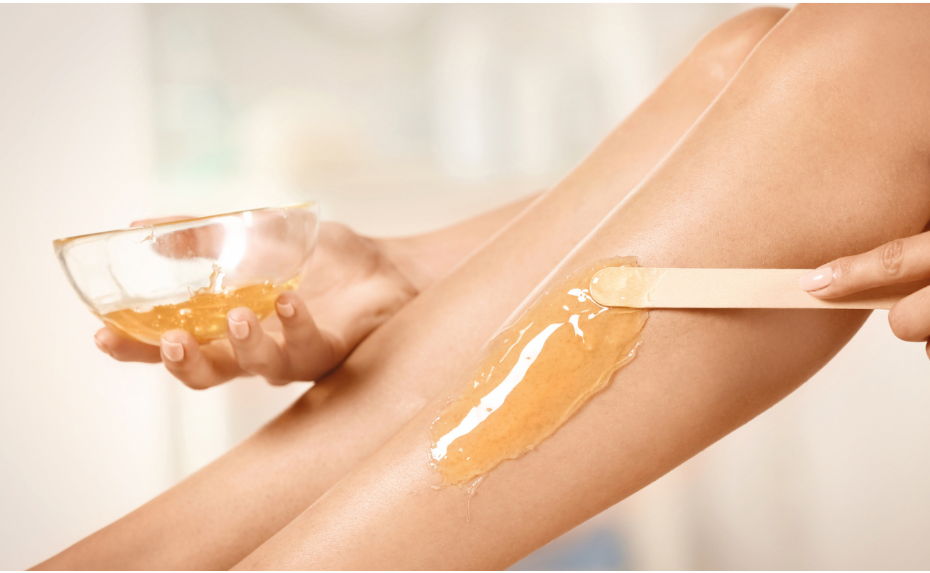 Person waxing their leg with a bowl of wax and wooden applicator.
