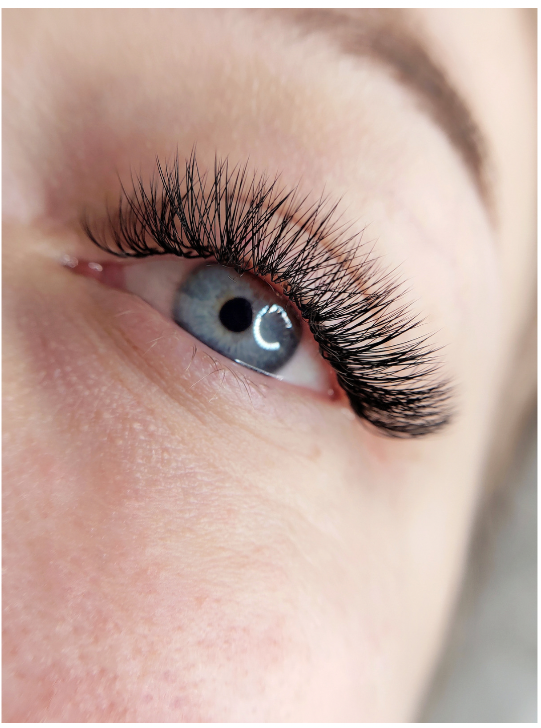 Close-up of a blue eye with thick, black eyelash extensions; fair skin.