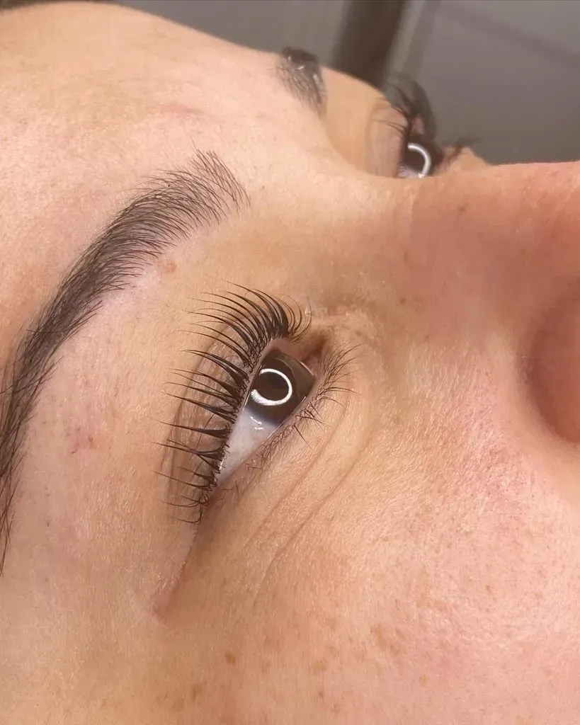 Close-up of a person's eye with lifted lashes and a full, dark eyebrow.