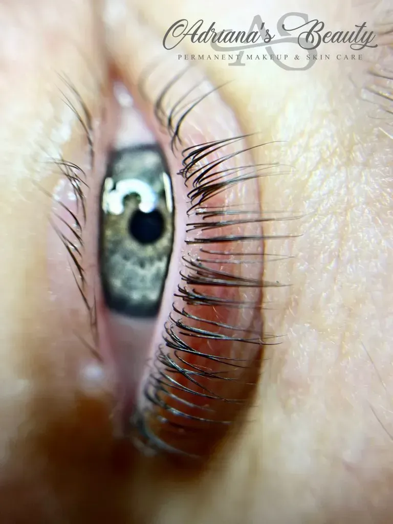 Close-up of an eye with lifted lashes, showing a light-colored iris. The setting seems to be an aesthetic spa.