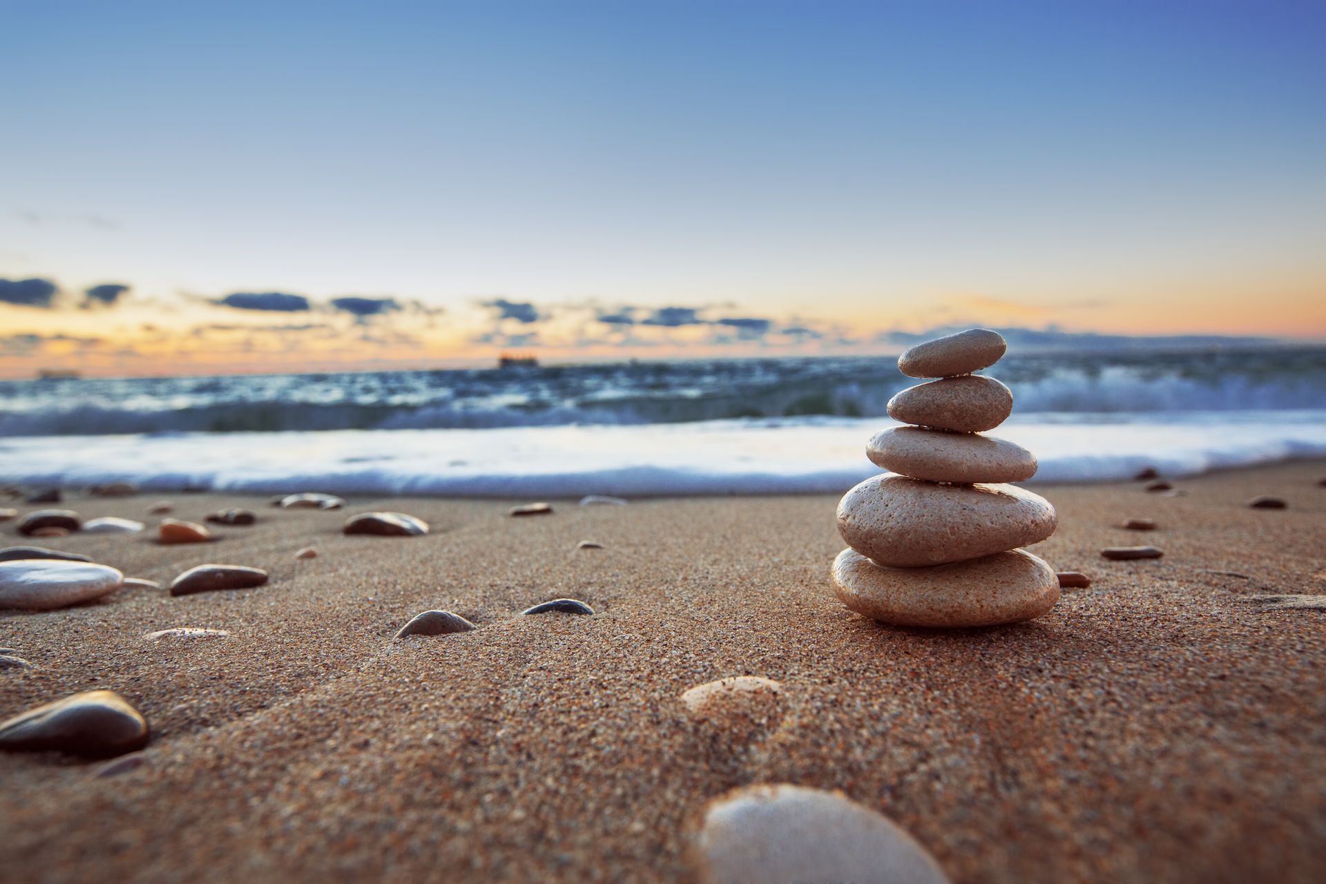 A calm beach at sunset with a stack of rocks on the sand.