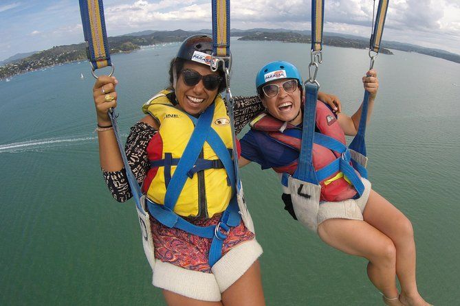 Two women are parasailing over a body of water.