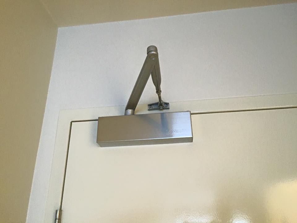 A stainless steel door closer is attached to a white door