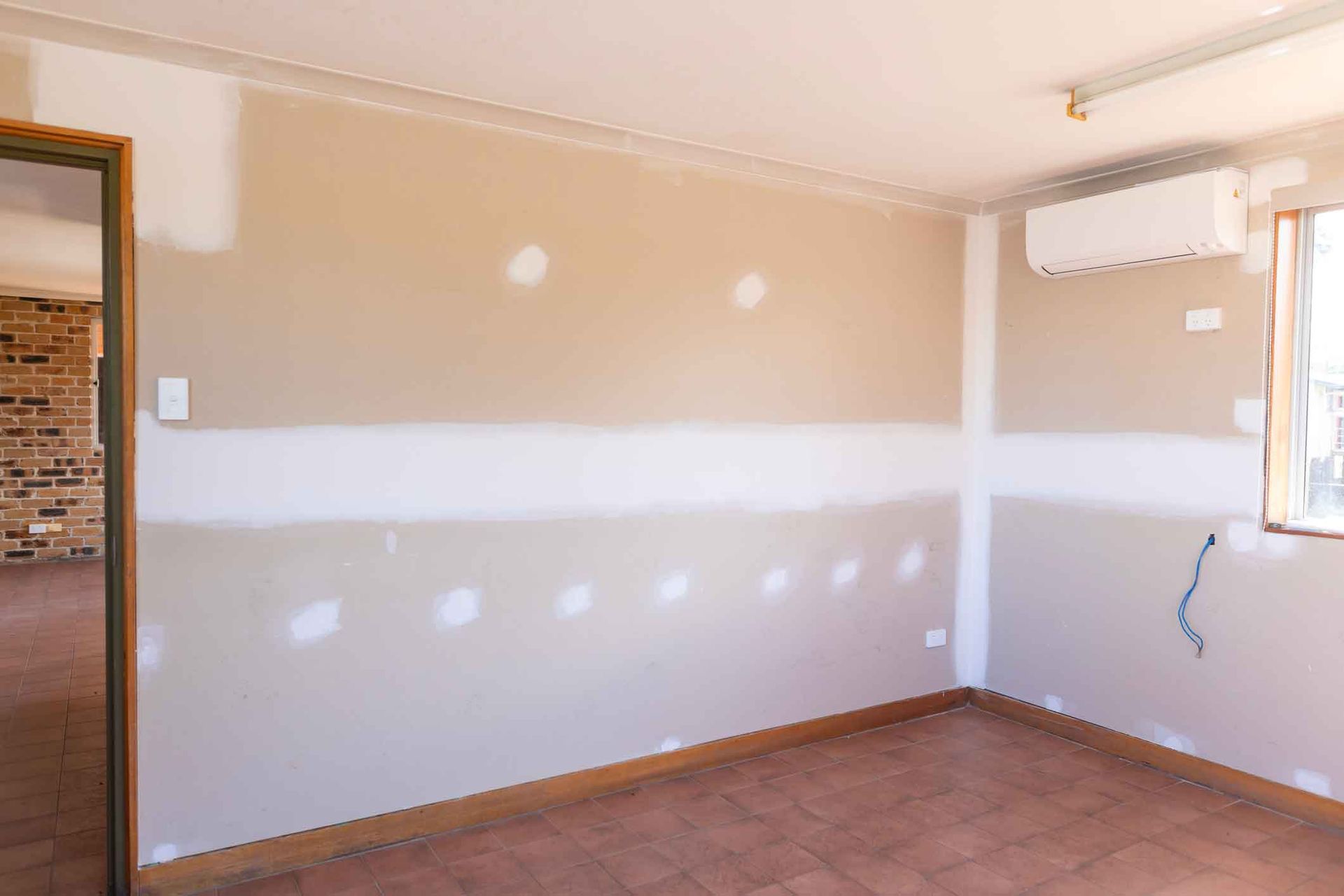 An empty room with a window and a fan on the wall.