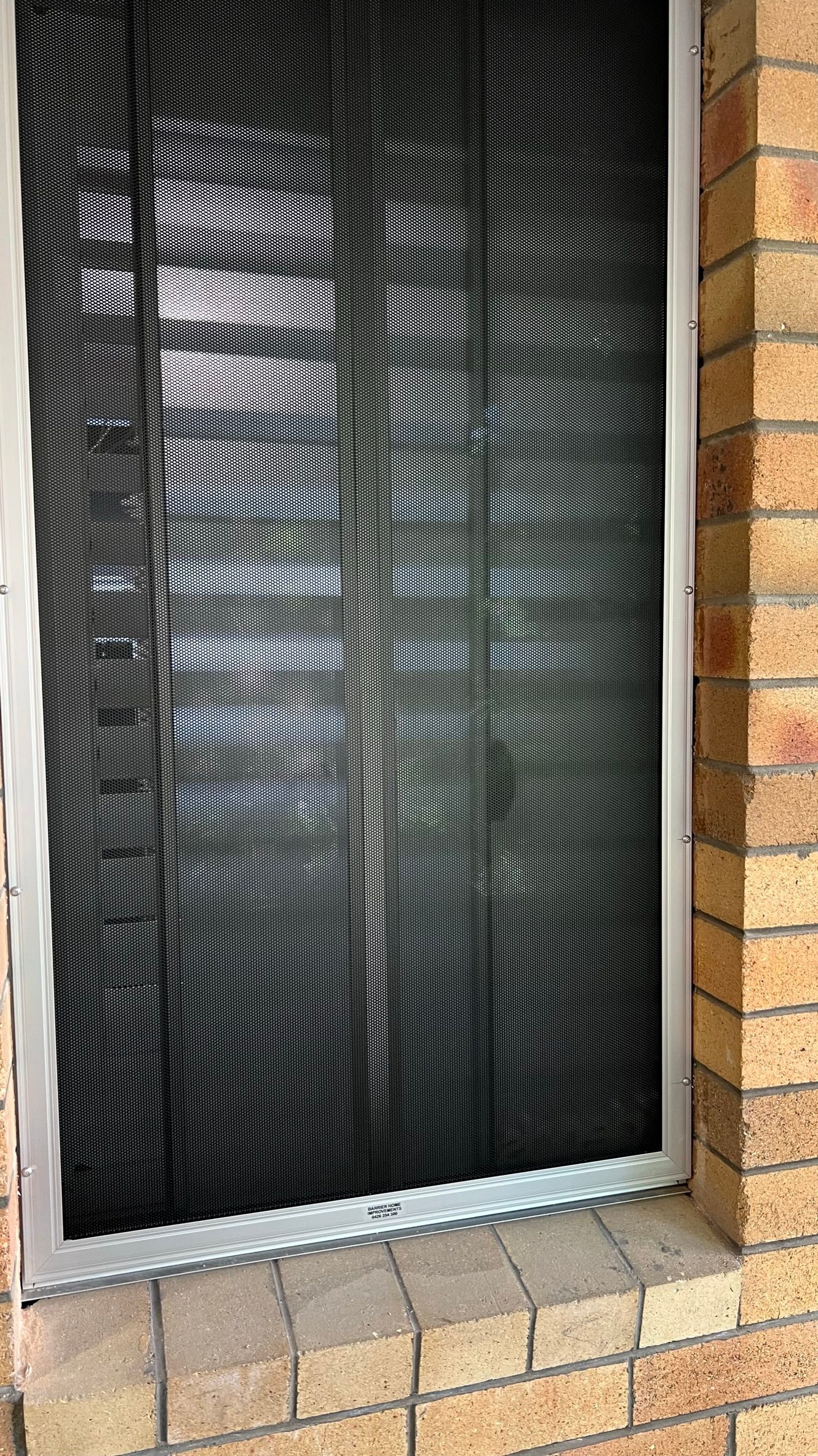 A sliding glass door with a black screen on it is on a brick wall next to a window.