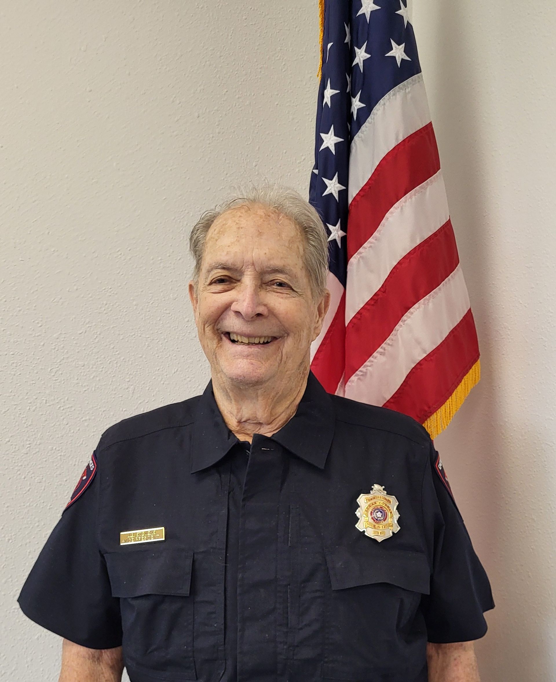 A man in a blue shirt is standing in front of an american flag.