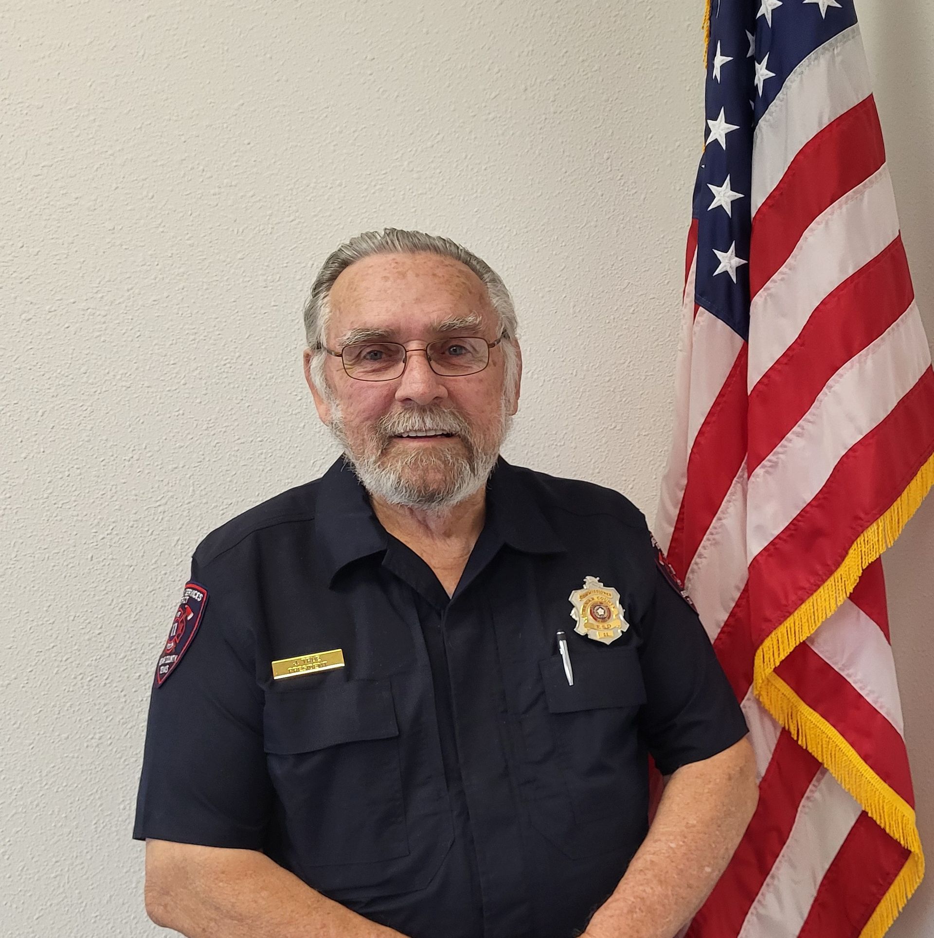 A man with a beard and glasses is standing in front of an american flag.