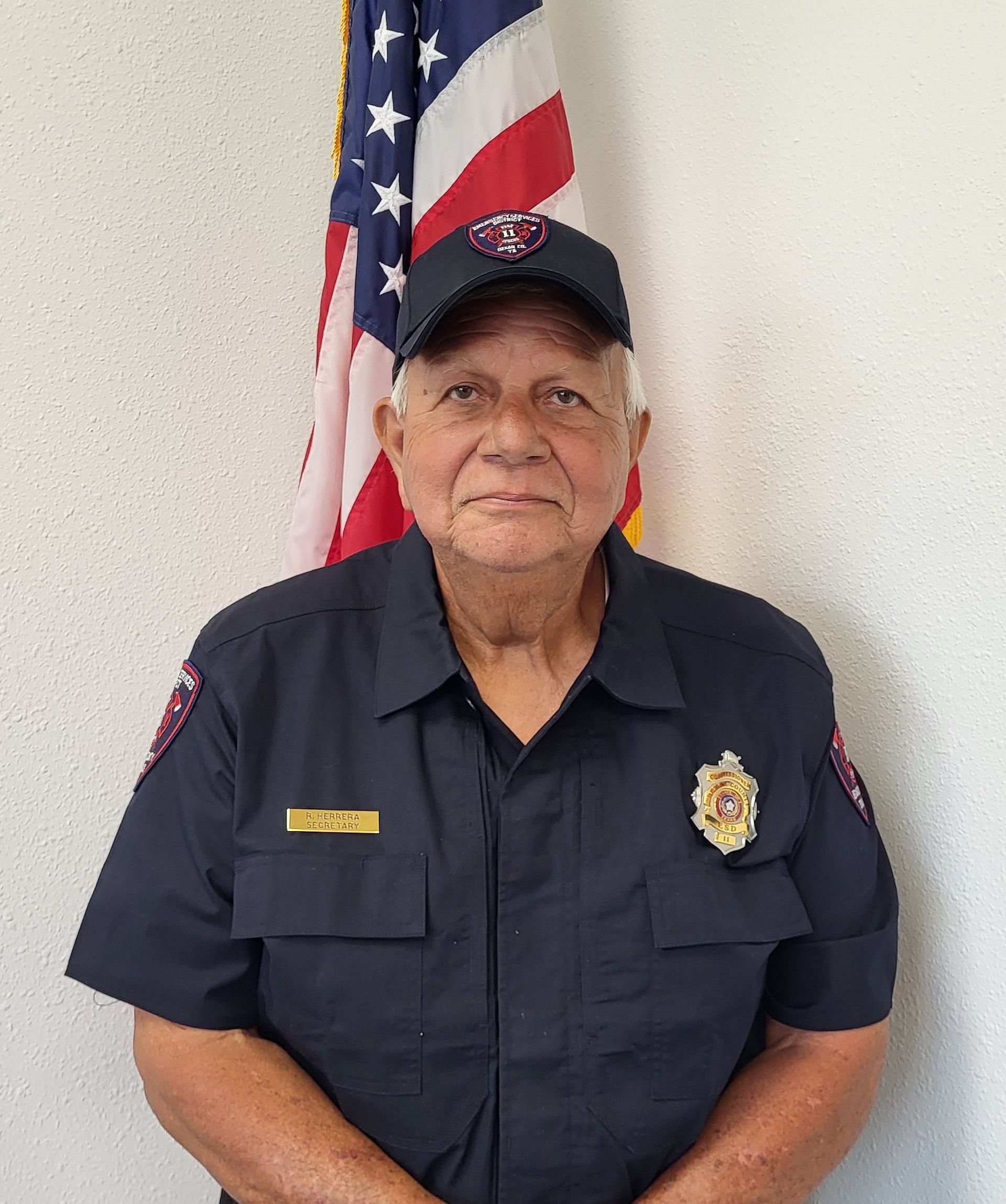 A man wearing a hat and a polo shirt is standing in front of an American flag
