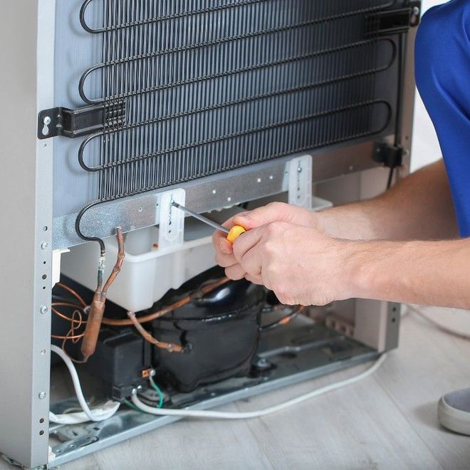 A person using a screwdriver to repair the rear panel and cooling components of a refrigerator.