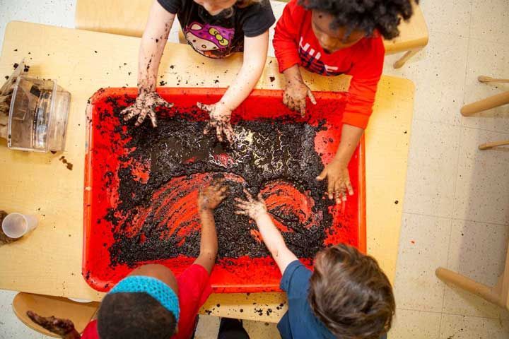 a group of children are playing with mud in a red tray .