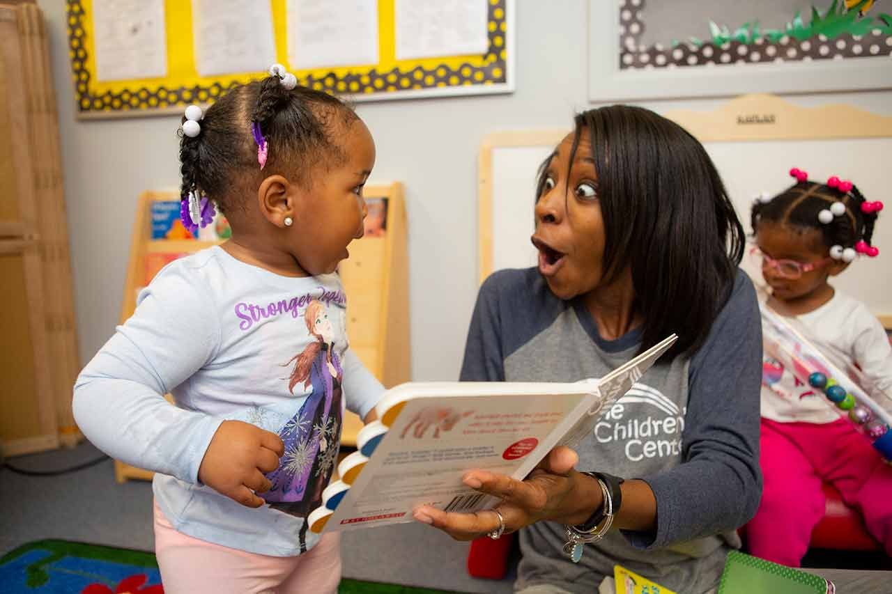 a woman in a children 's center shirt reads a book to a little girl