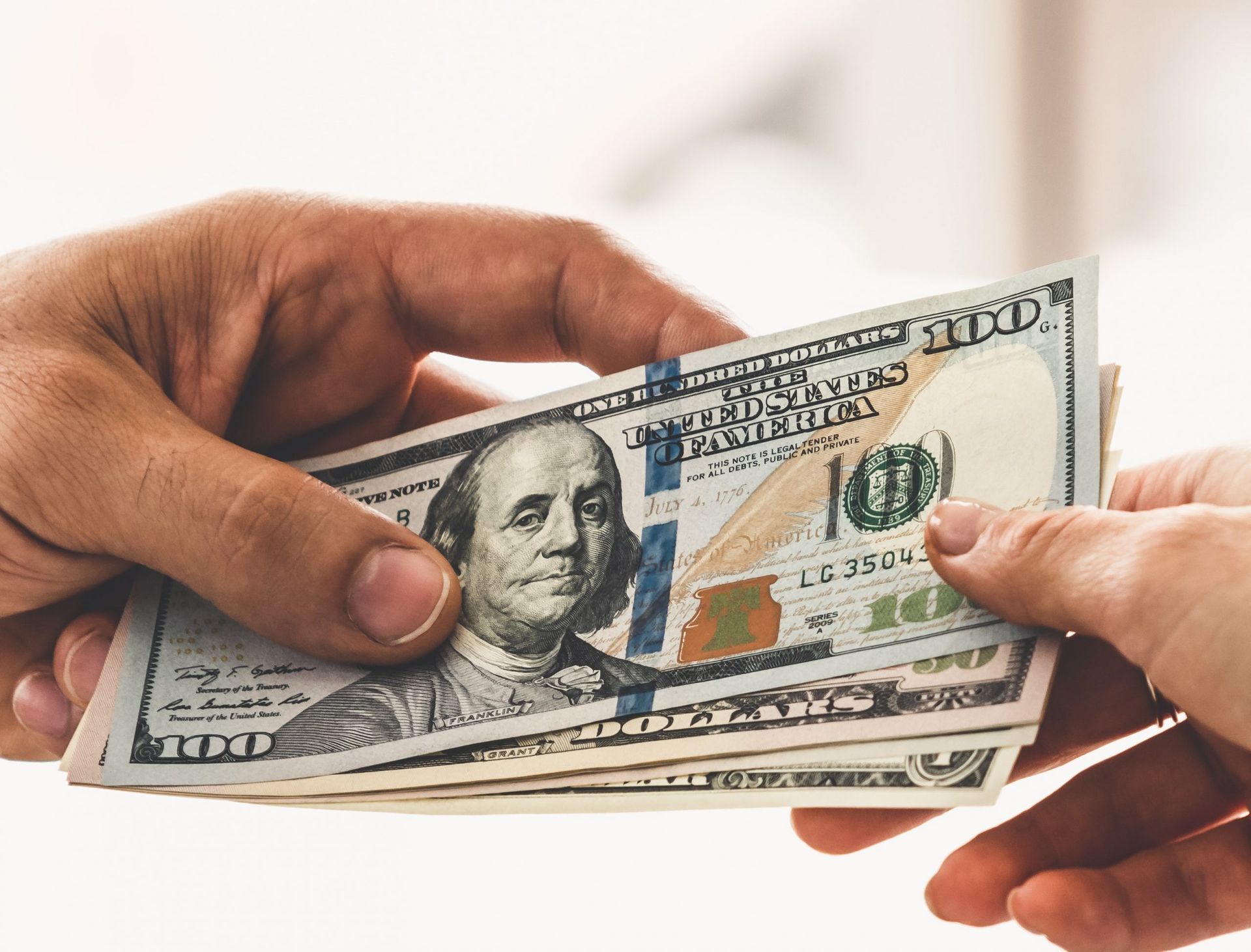 Hands exchanging a stack of $100 bills.