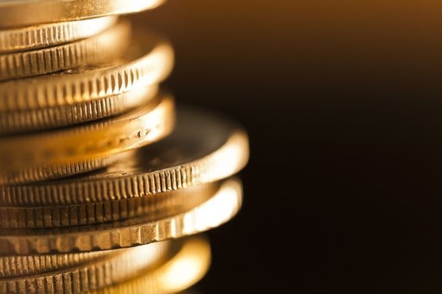 Stack of gold coins, close-up, against a dark background.
