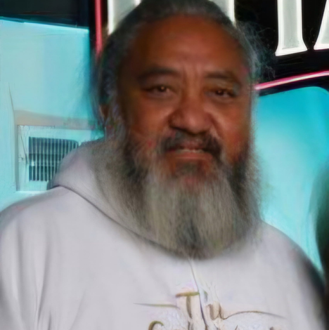 Man with long gray beard in black and white plaid shirt, autumn foliage background.