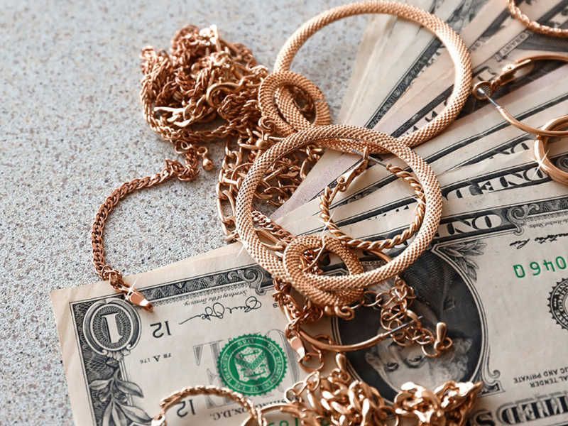 Gold jewelry and U.S. dollar bills on a light-colored surface.