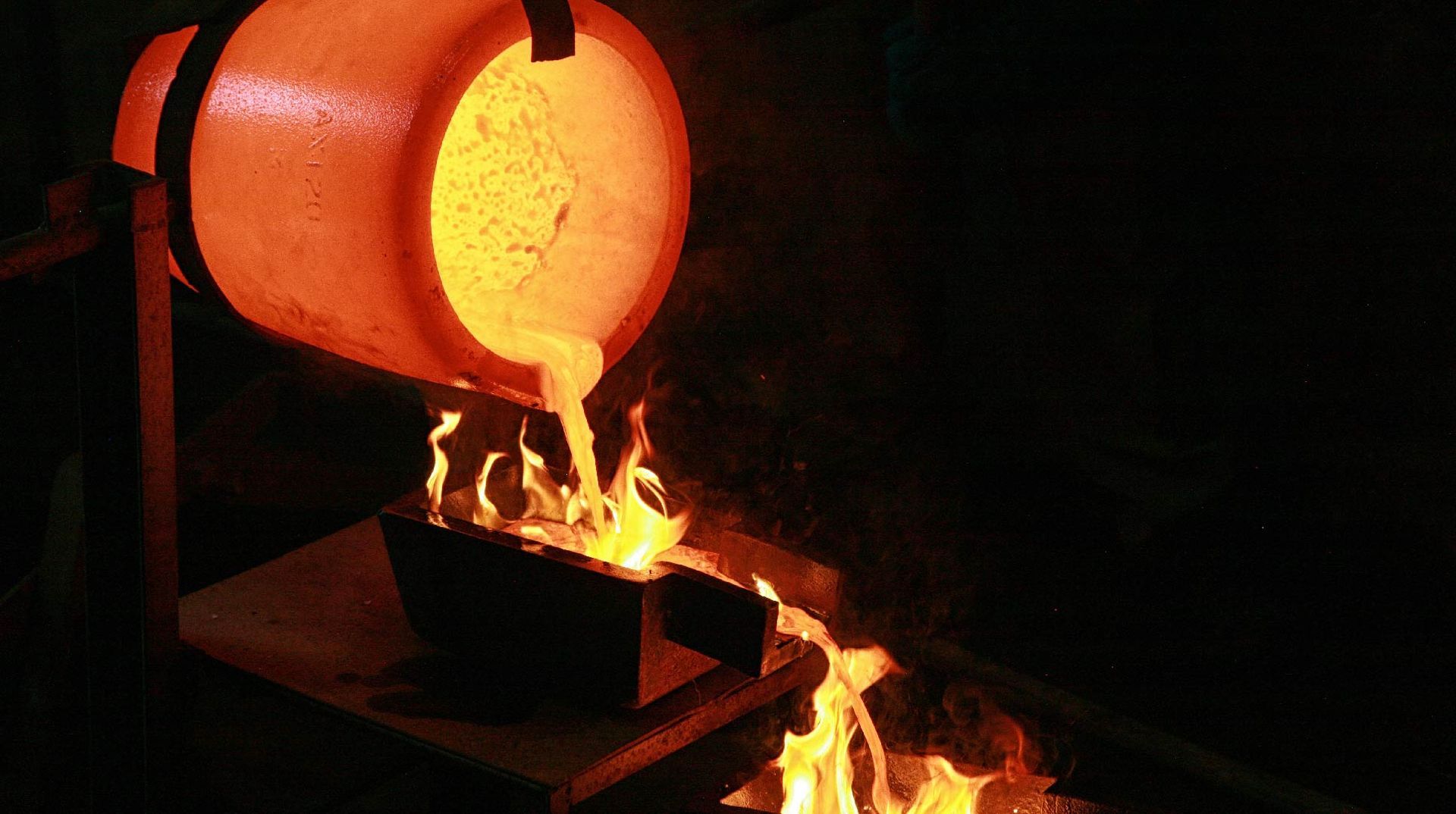 Molten metal pouring from a glowing orange crucible into a mold; flames at the base.