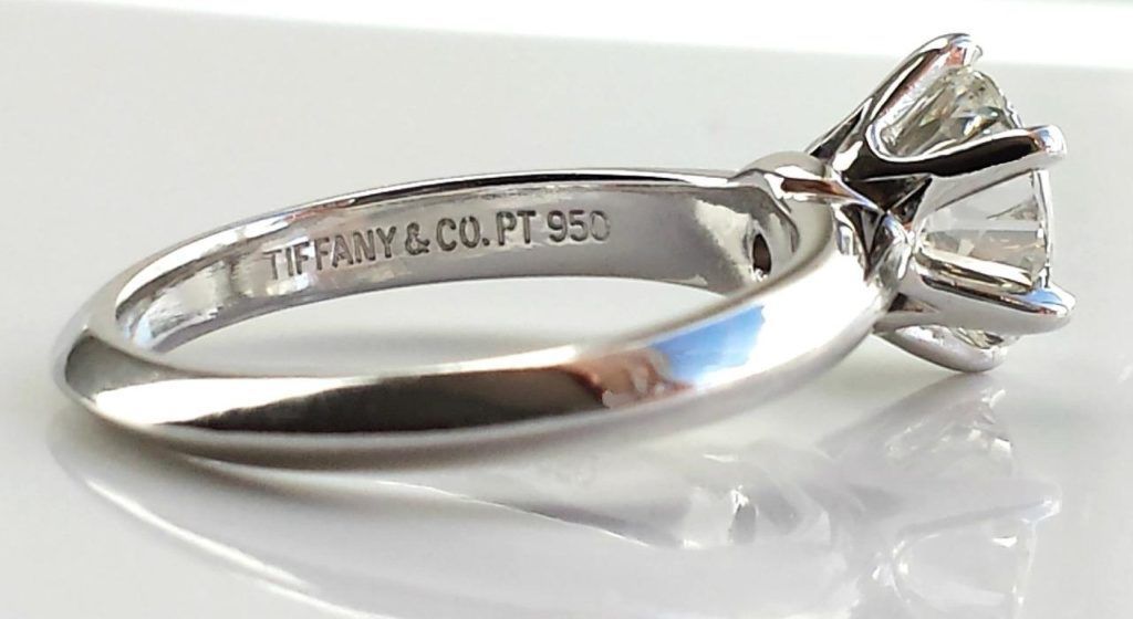 Tiffany & Co. diamond engagement ring on a reflective white surface. Platinum band, engraved logo and PT 950.