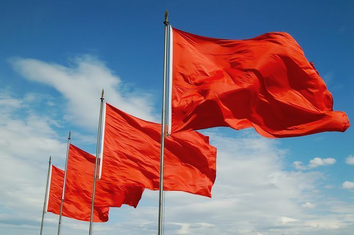 Row of bright red flags waving against a blue sky with scattered clouds.