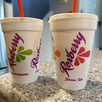 Two Roxberry smoothies in white cups with orange straws on a counter.