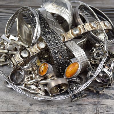 Pile of silver jewelry, including rings, bracelets, and necklaces with amber accents, on a wooden surface.