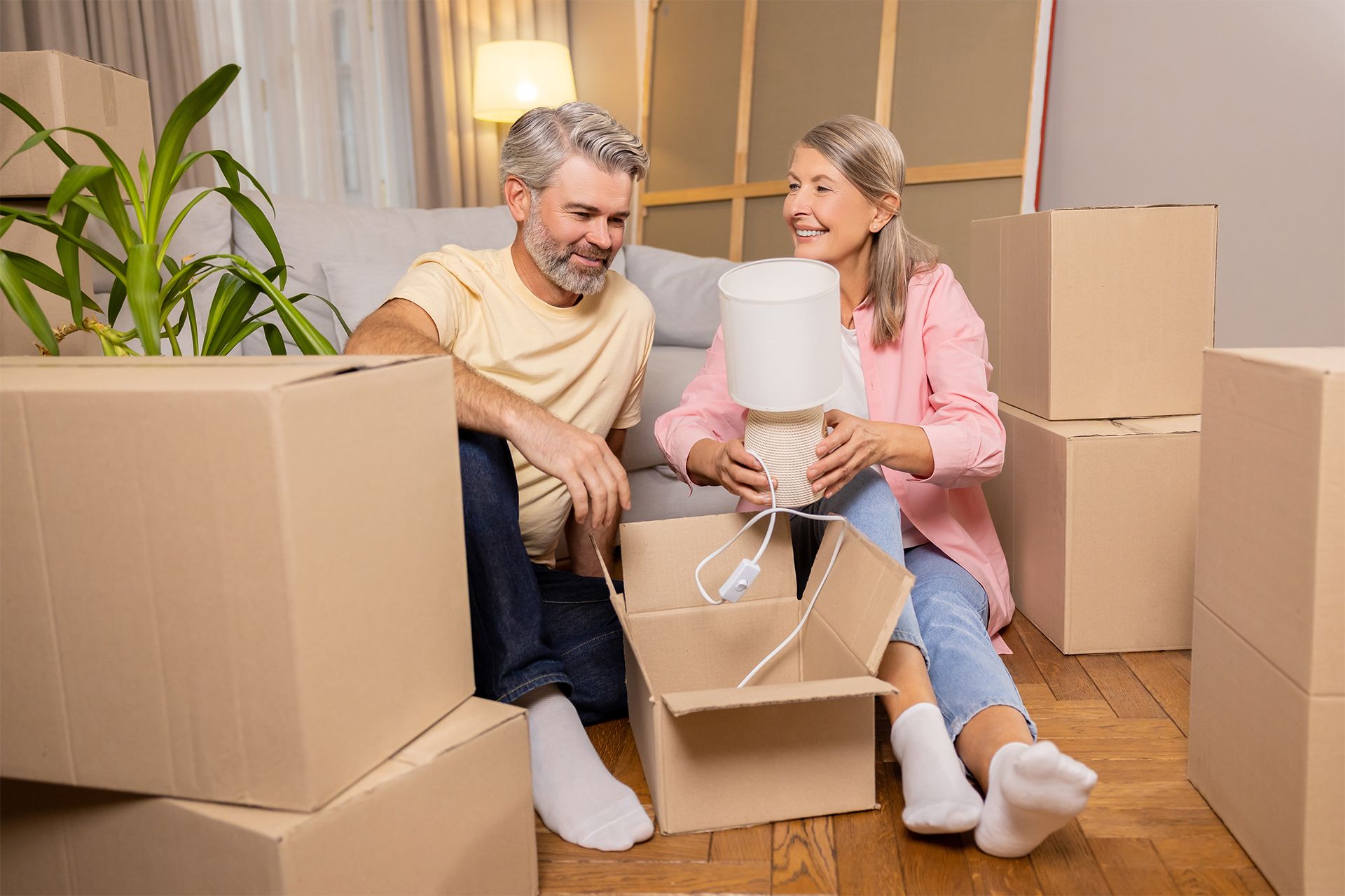 Senior couple unpacking boxes, sitting on floor in new home.