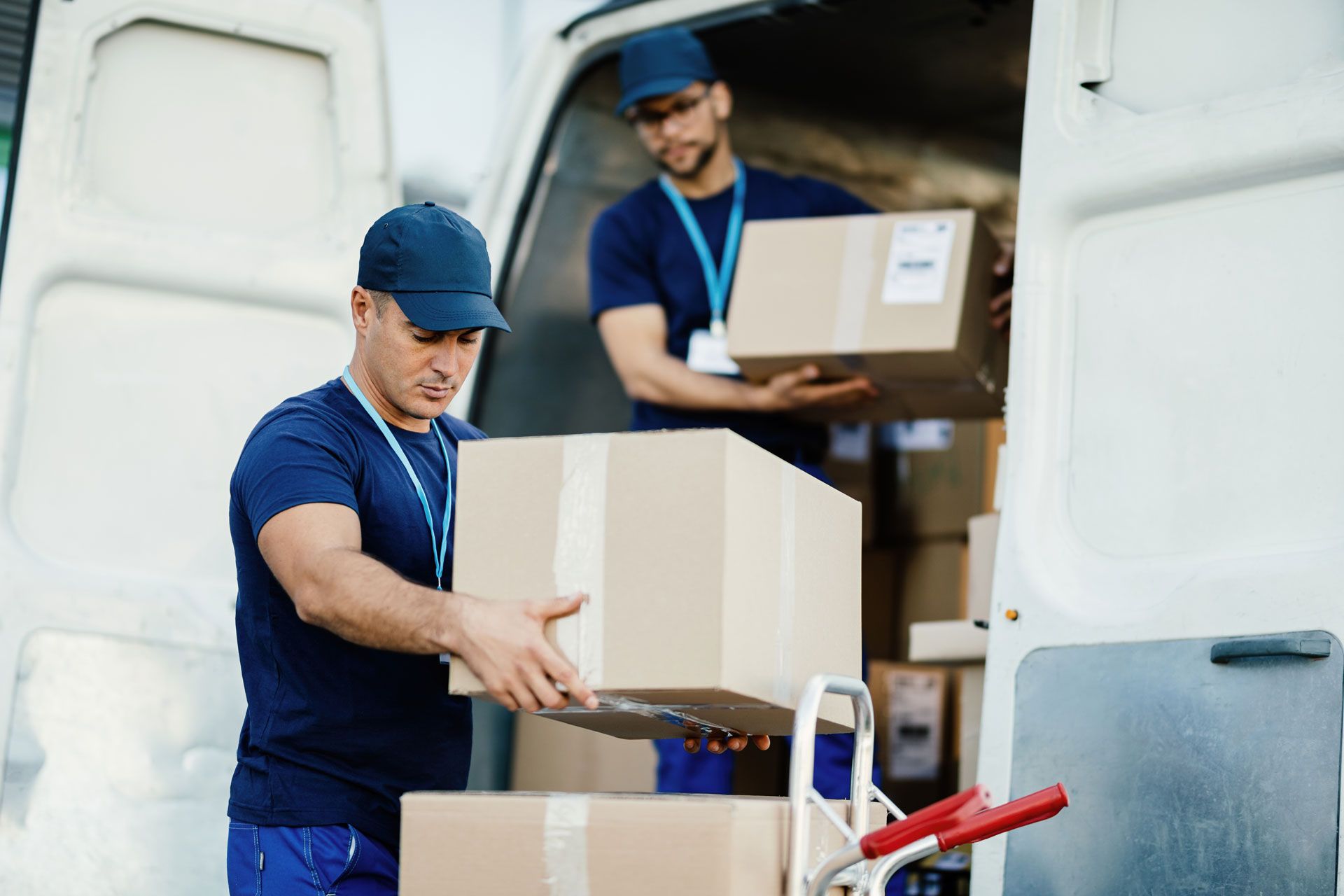 Two delivery workers unloading cardboard boxes from a white van