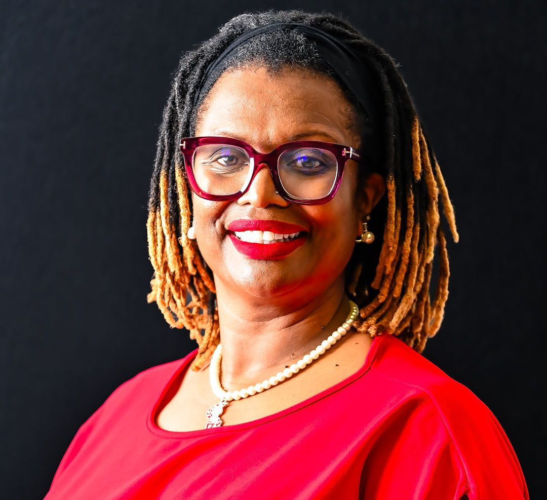 Woman with glasses, red dress, smiling, against a black background.
