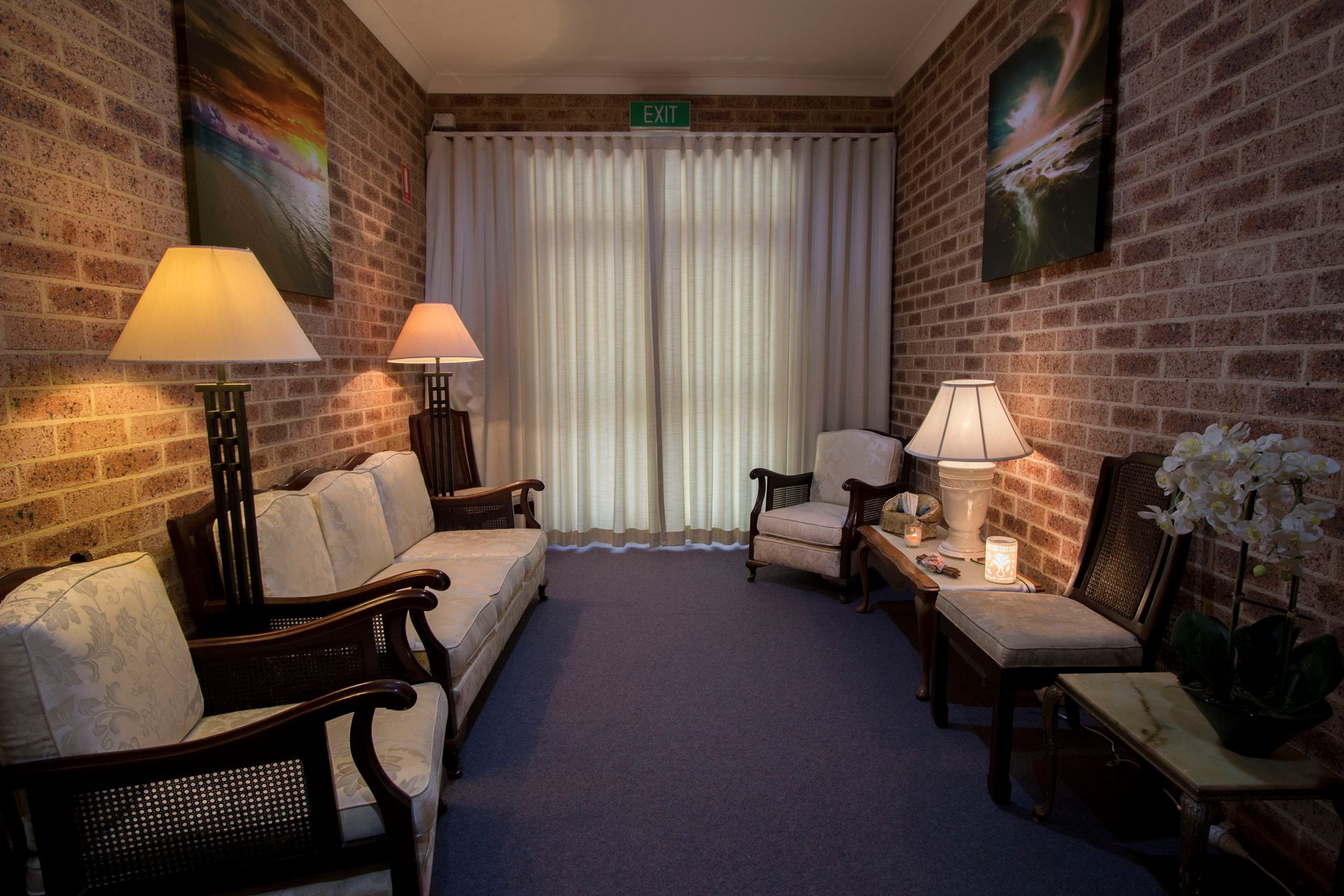 Cozy waiting area with brick walls, sofas, armchairs, lamps, and curtains, with artwork.