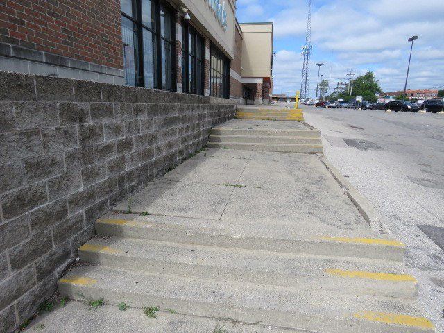 Exterior steps and  sidewalk along a brick building but no guardrail for safety