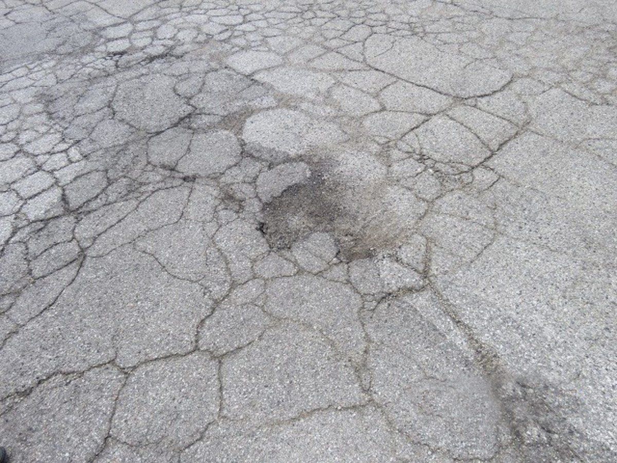 Blacktop pavement with a spideweb of cracks creating uneven walking surface