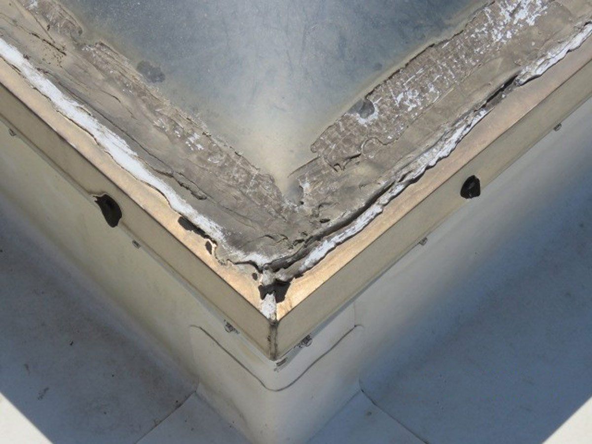 Closeup view of a roof skylight that is old and showing cracks in the caulking and sealing allowing leakage