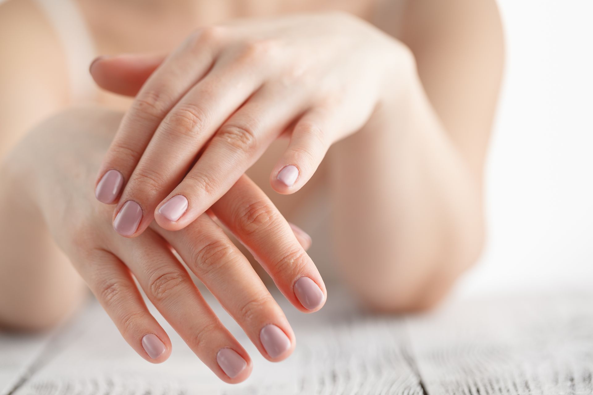 Hands with pale pink nails resting on a white wooden surface