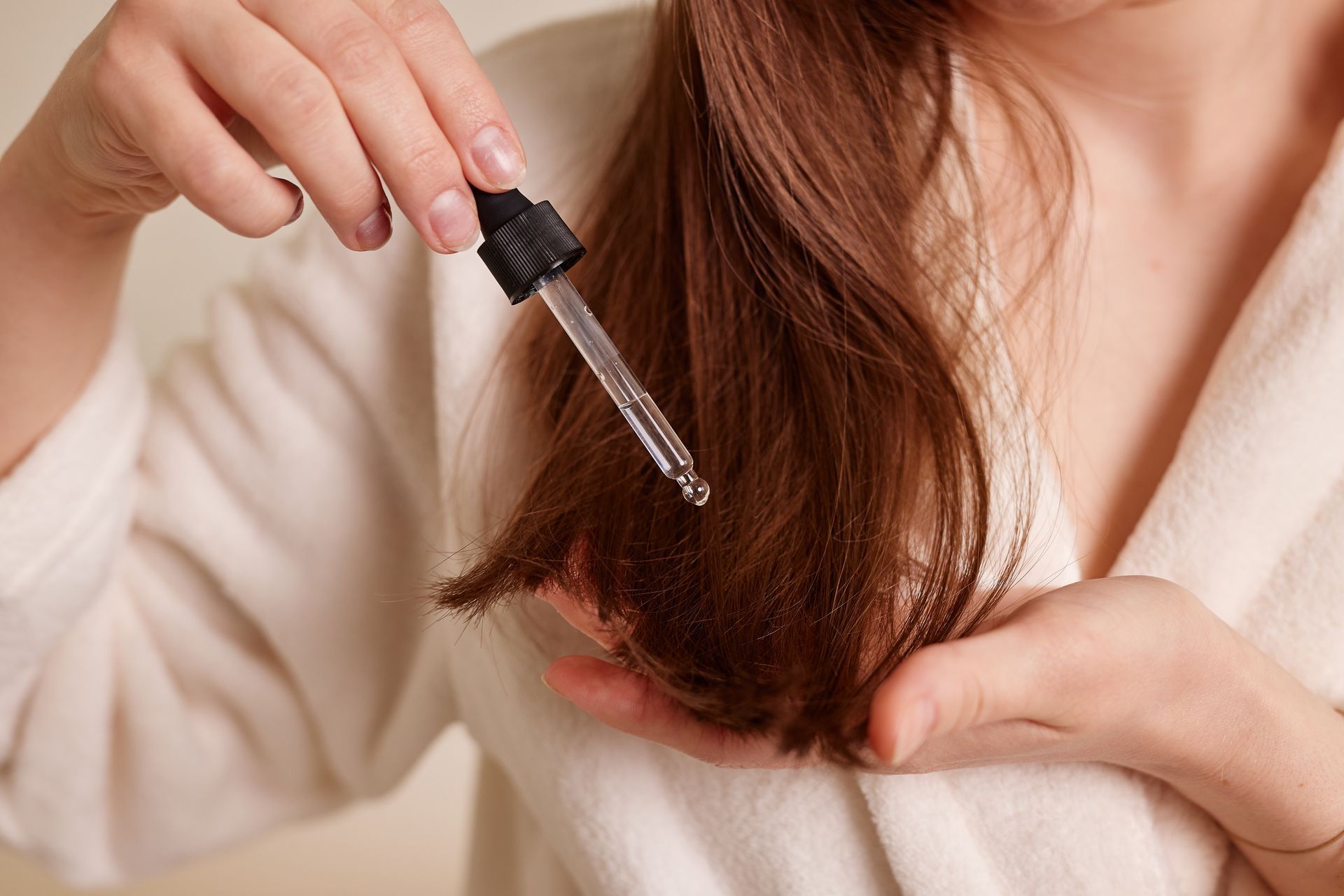 Applying hair oil to the ends of brown hair with a dropper