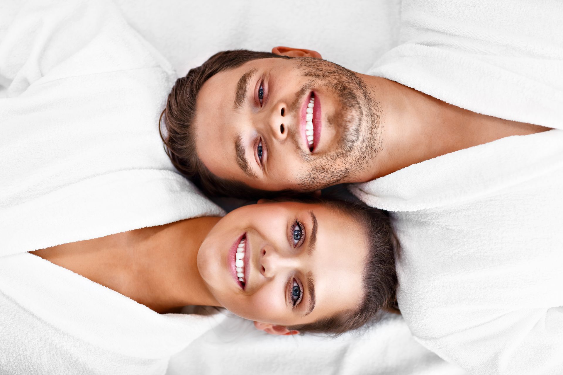 A man and a woman are laying next to each other on a bed and smiling.