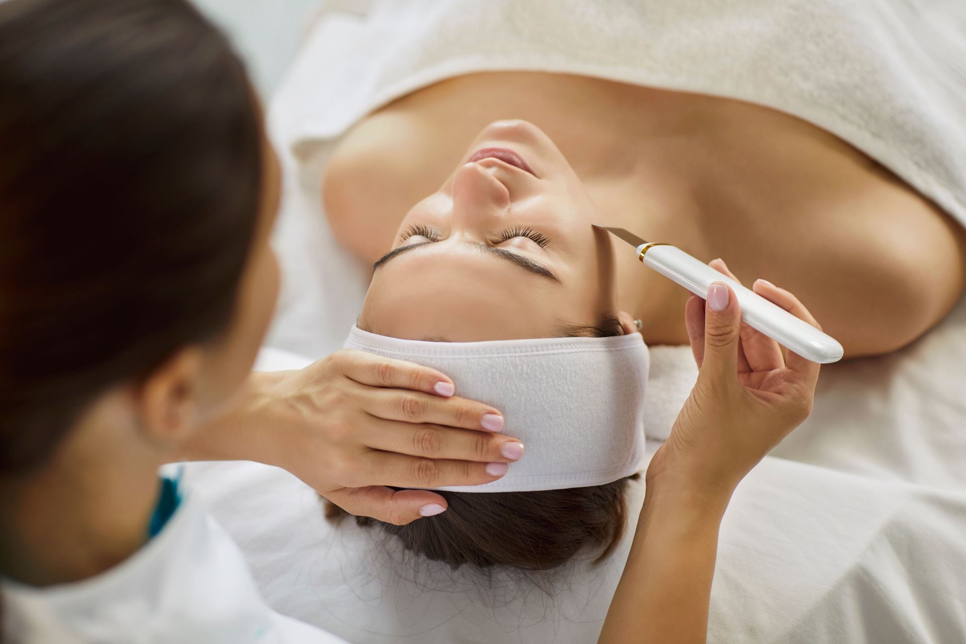 Spa facial treatment with woman lying down while an aesthetician applies cream with a brush