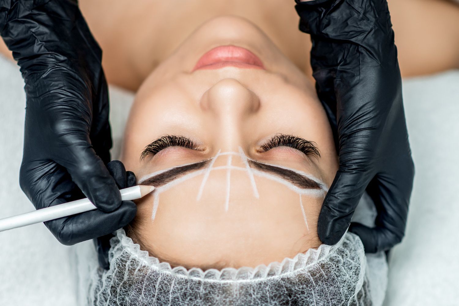 A woman is getting her eyebrows drawn by a tattoo artist.