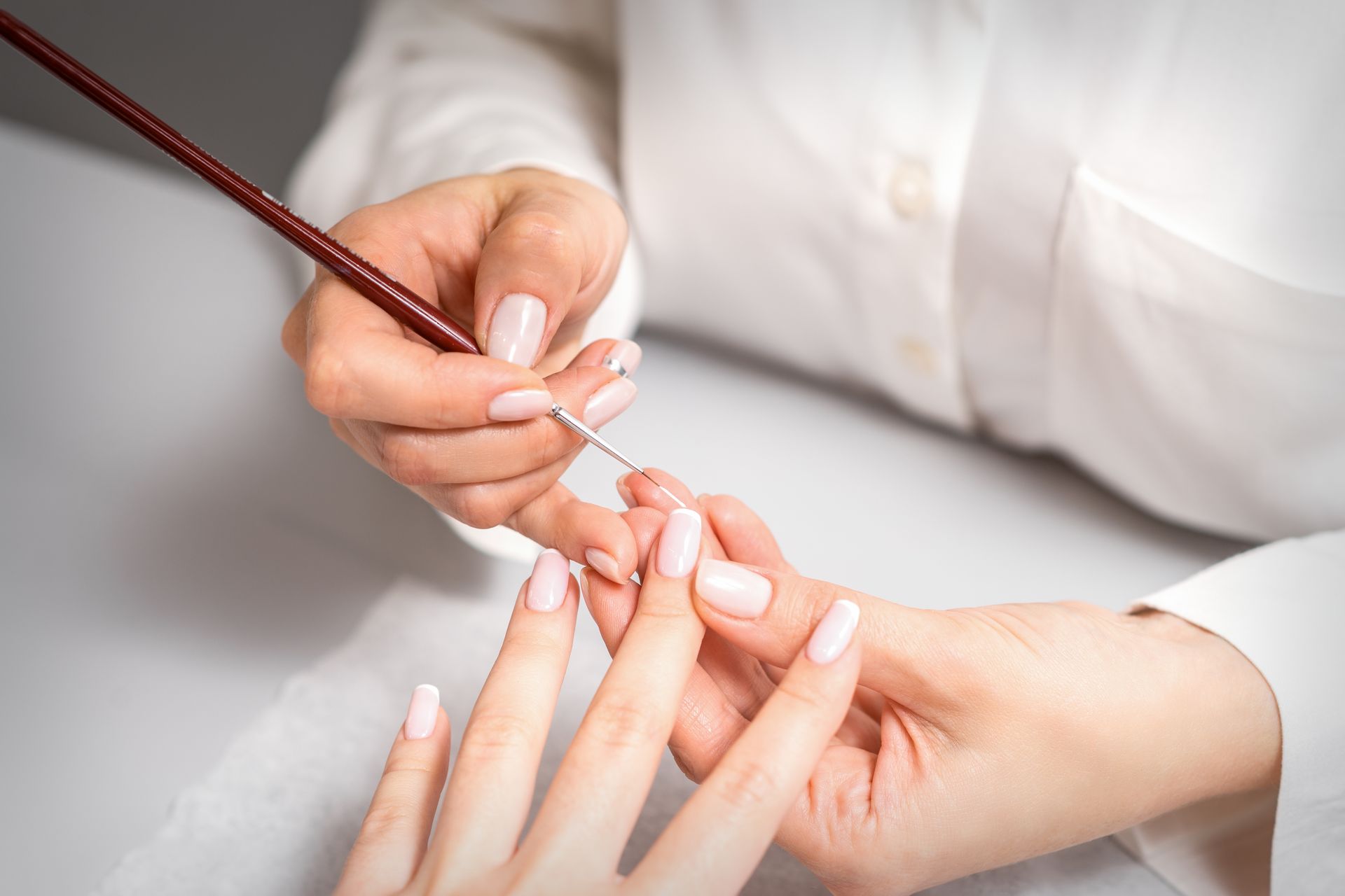 Manicurist painting a fingernail with a brush.