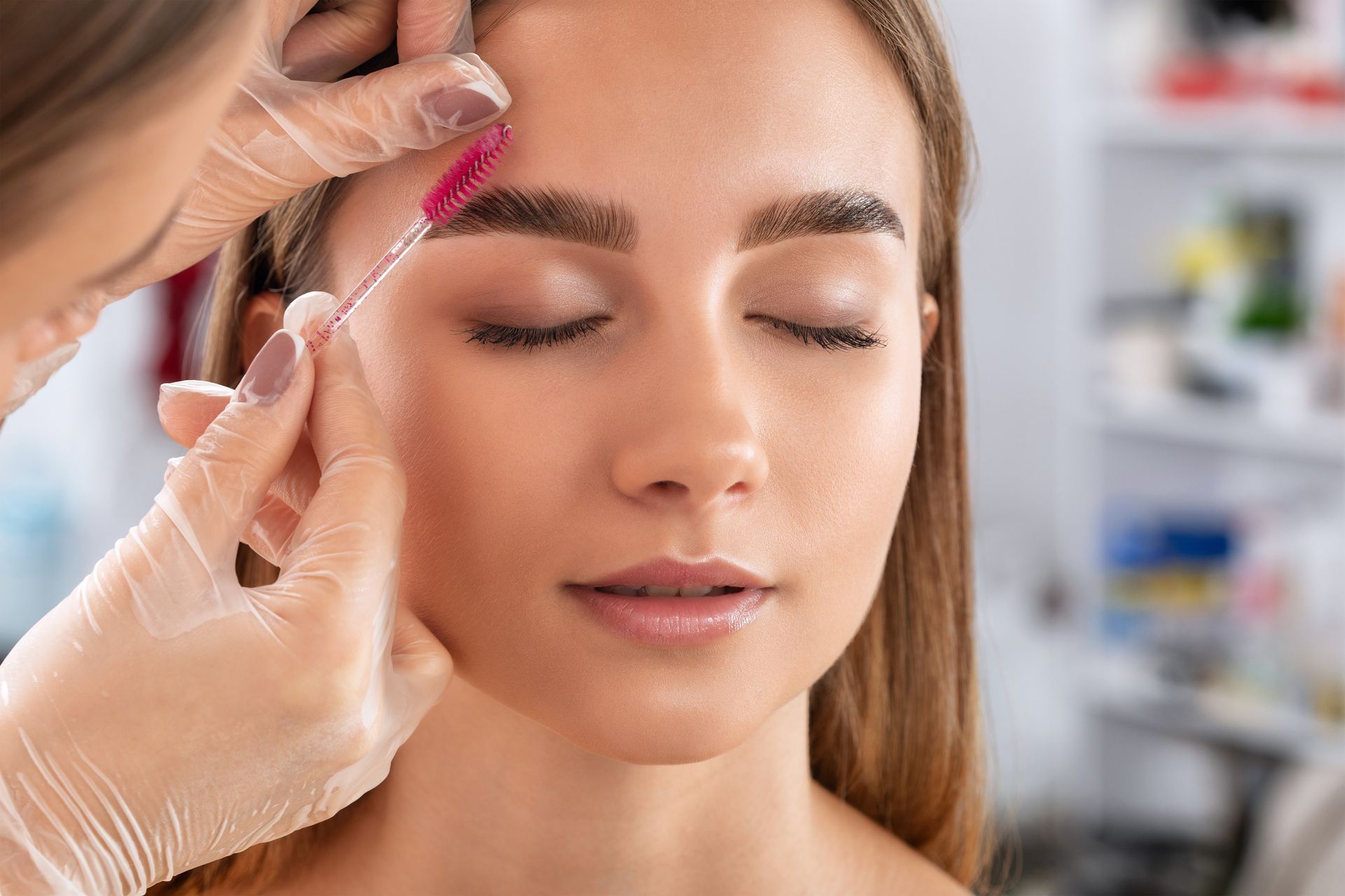 Woman having her eyebrow brushed by someone wearing gloves, indoors.