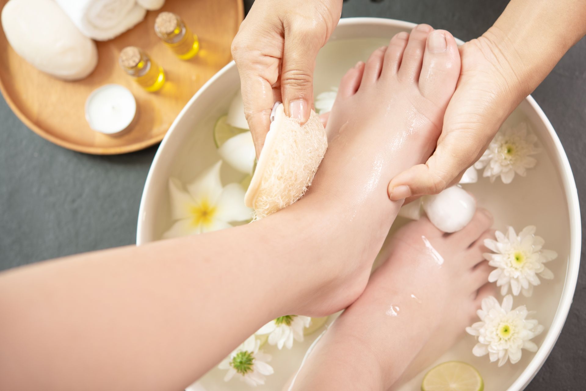 Foot spa treatment: feet soaking in water with flowers; hand holding a washcloth.