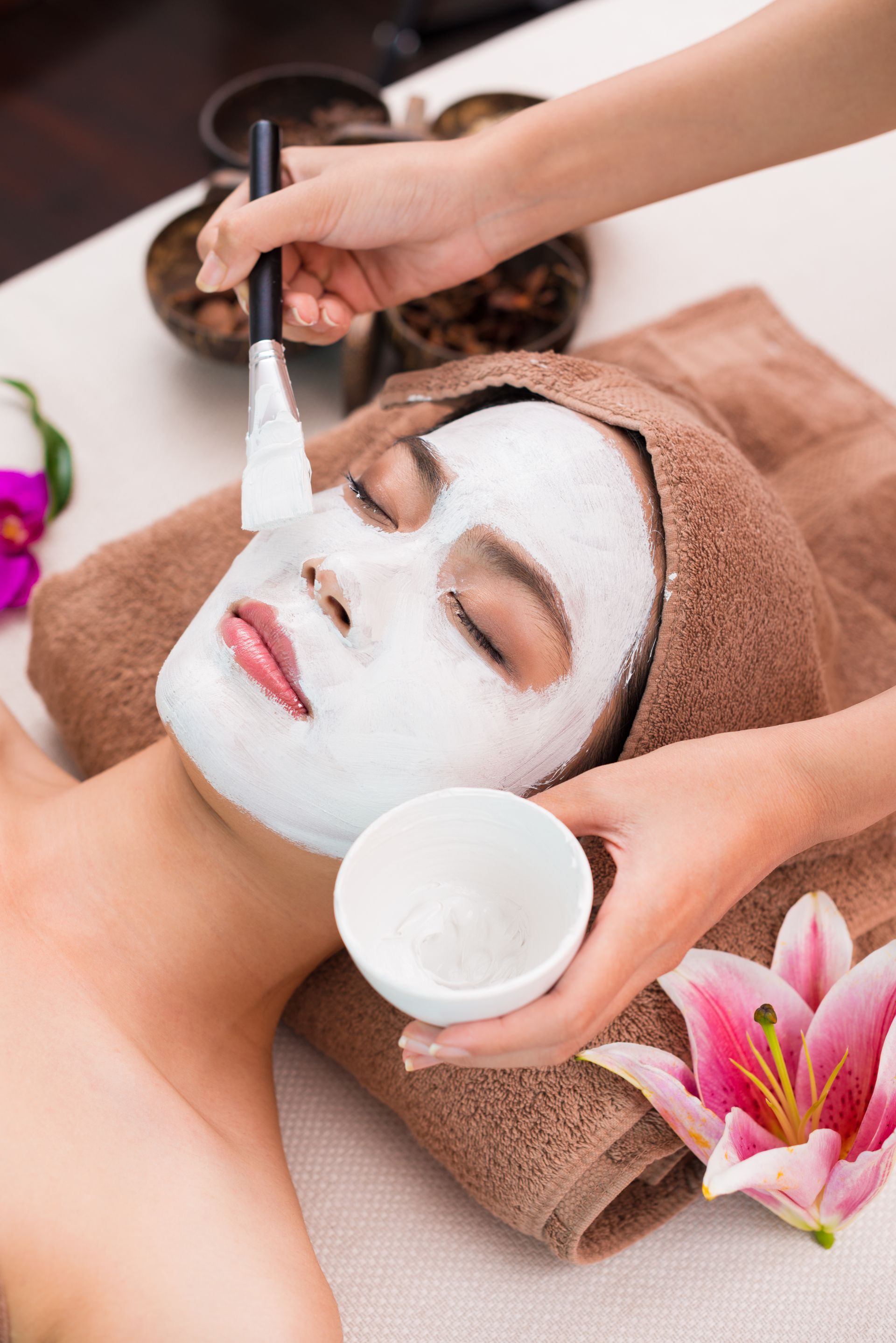 A woman is getting a white mask on her face at a spa.