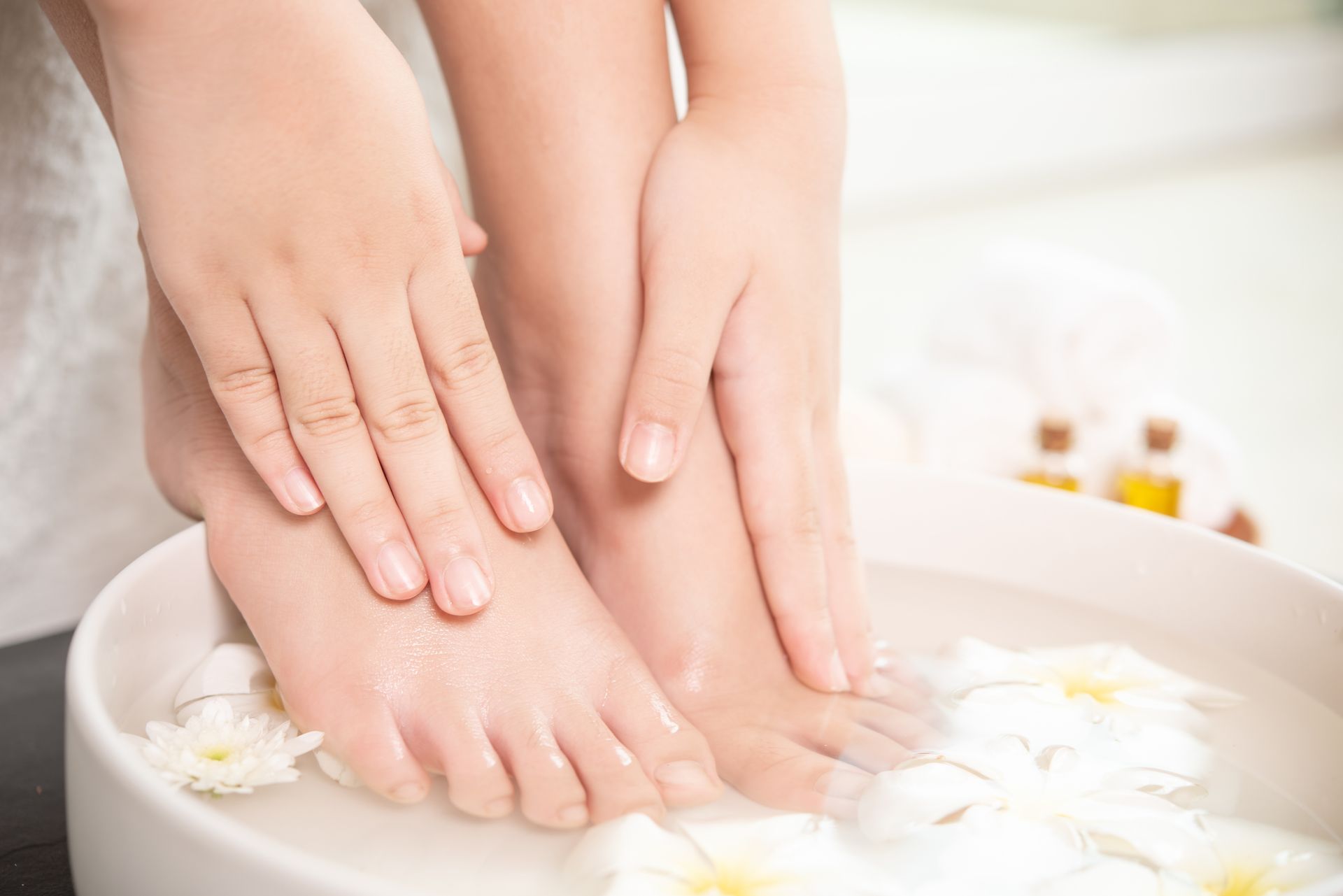 A person is washing their feet in a bowl of water with flowers.