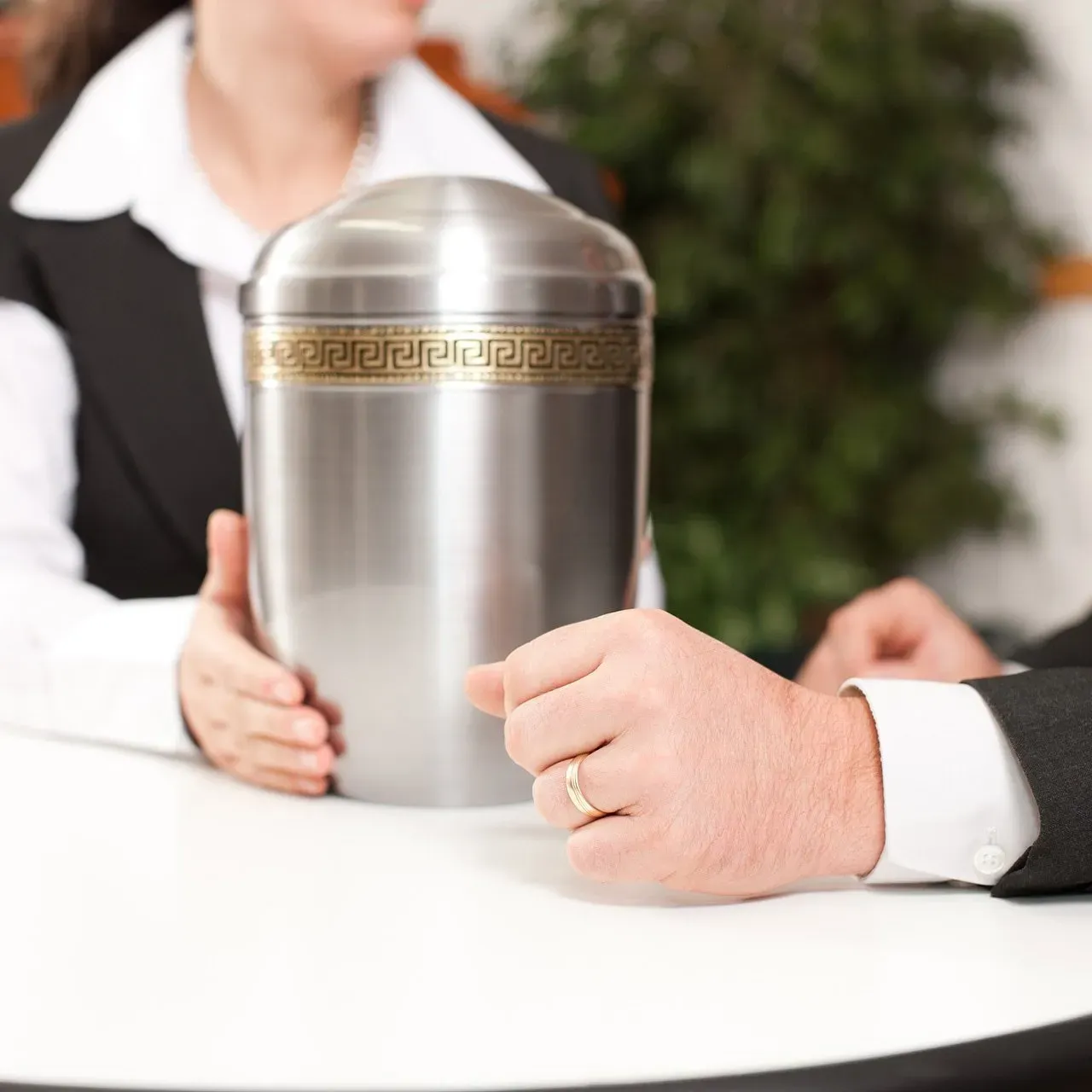 a man and a woman are sitting at a table holding a silver urn