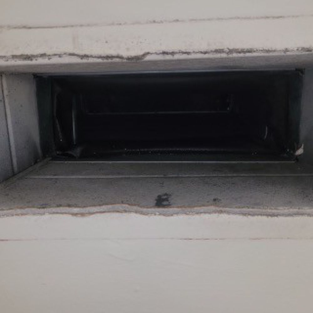 Man in blue overalls and mask using a tool to work on a ceiling.