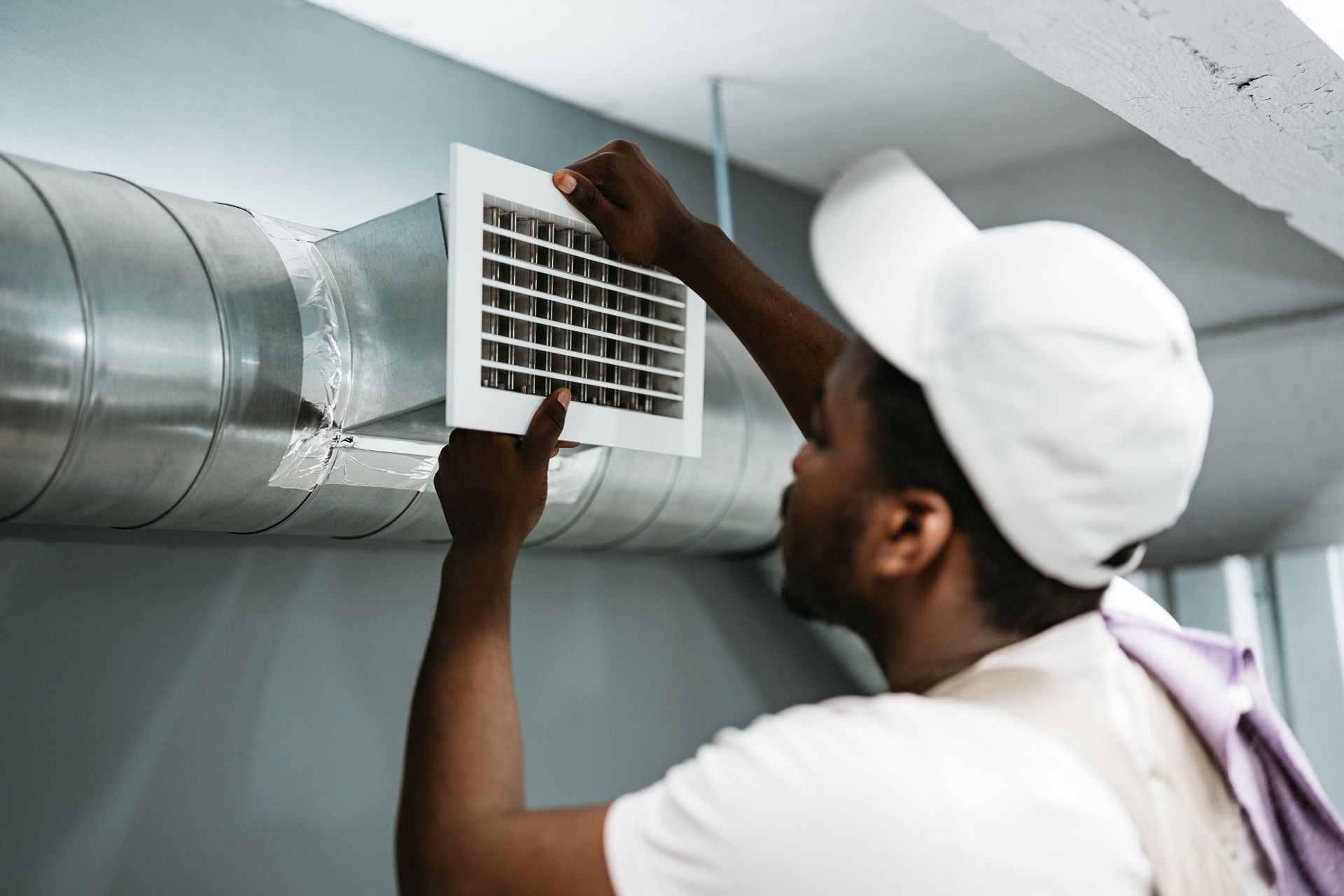 Person in white cap installing a vent cover on ductwork.