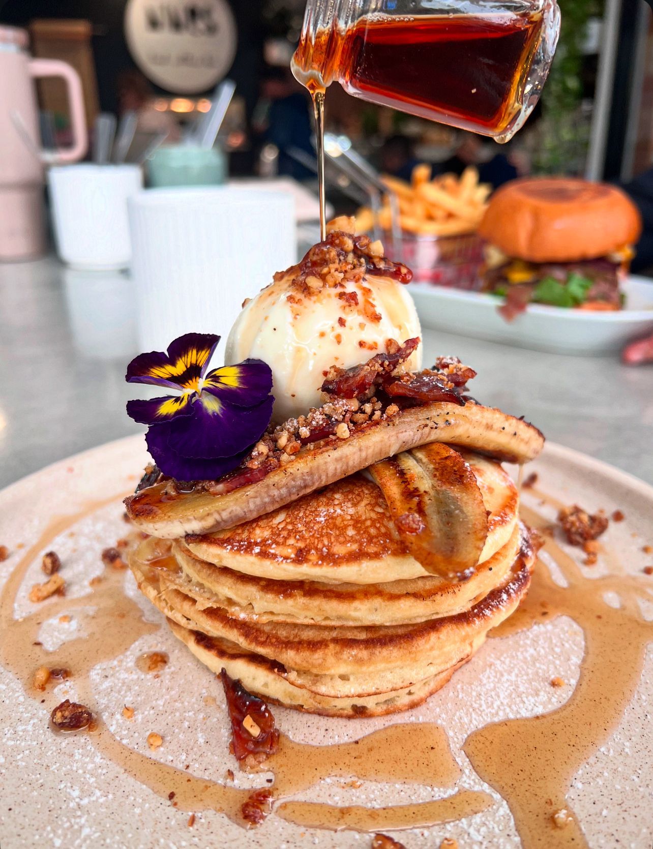 A stack of pancakes with ice cream and syrup being poured on top.