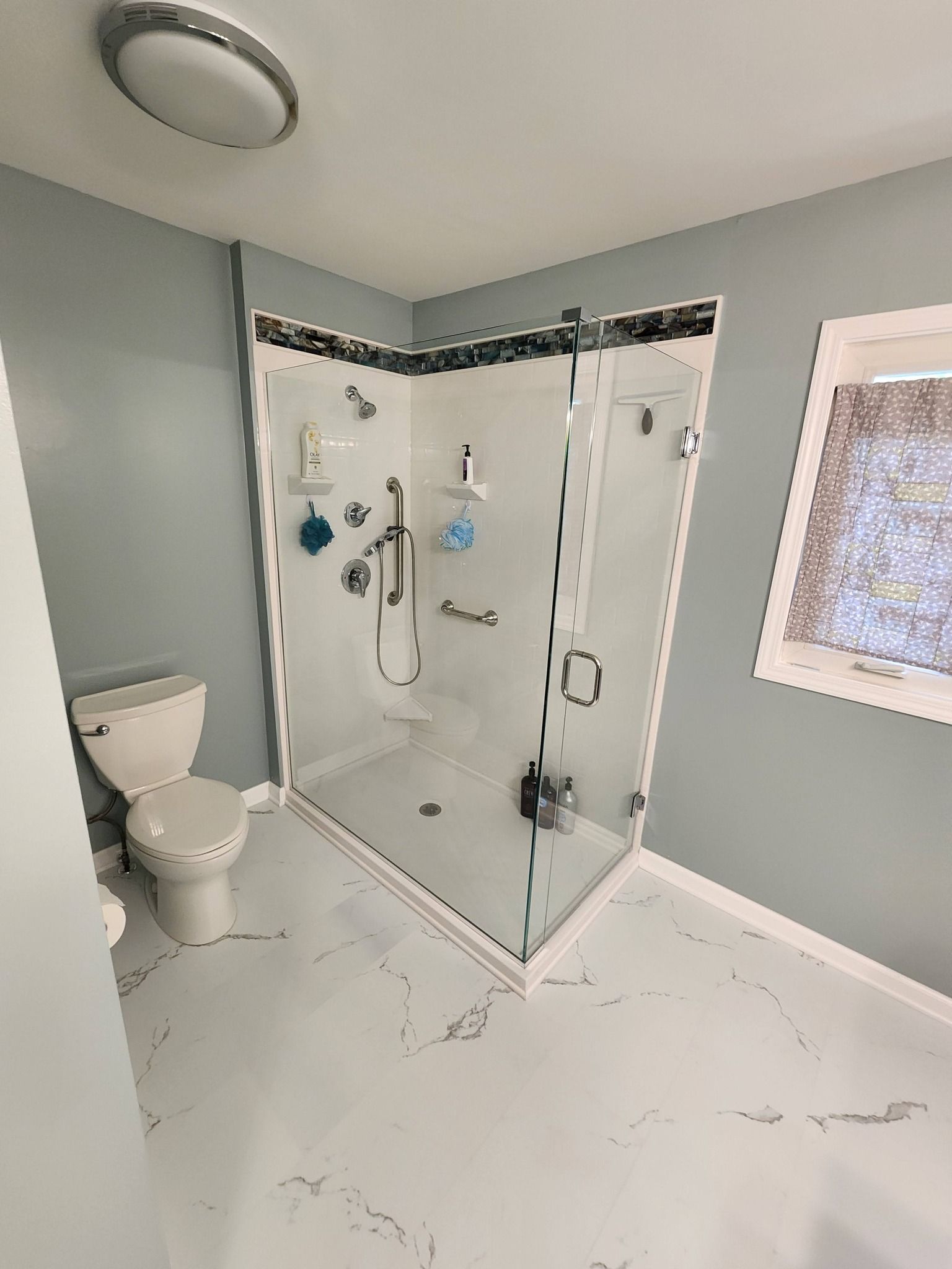 Bathroom with a corner shower, toilet, window, light fixture, and light blue walls.