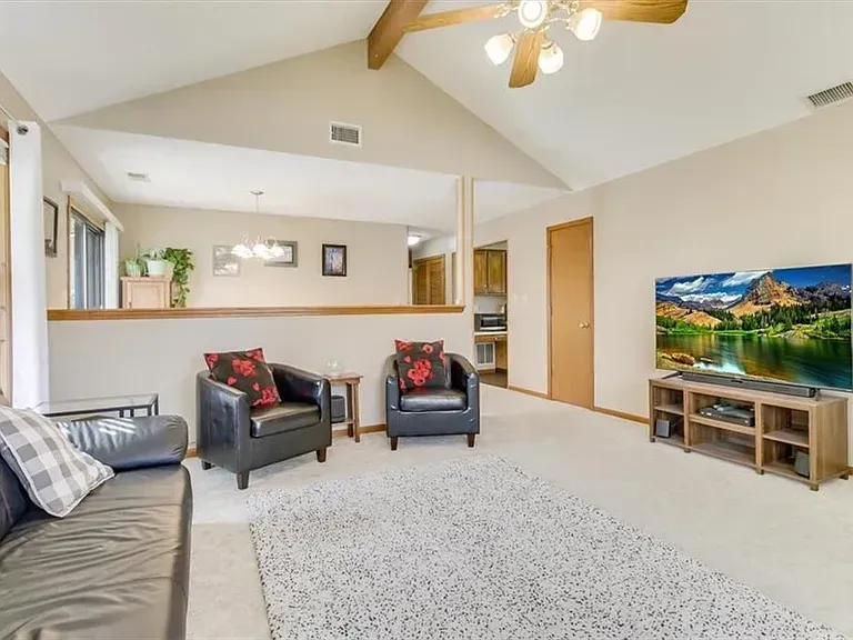 Living room with a large TV, two black armchairs, and a white fluffy rug.